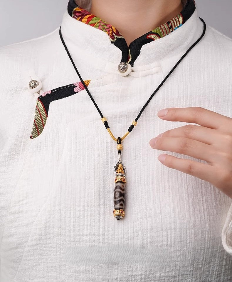 Model wearing golden deity dzi pendant on chest over traditional outfit